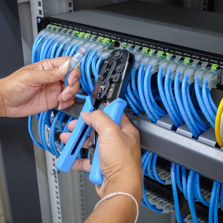 Smart Home and Building Networking and Wi-Fi for a hybrid workplace hand of system administrator with network cable connected to patch panel of network gigabit switch and crimping pliers tool